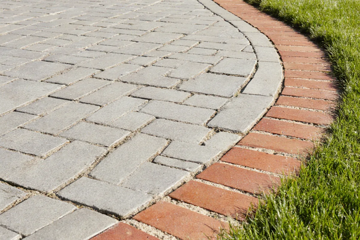 Freshly cleaned pale block paved driveway with a curved red border beside a lawn