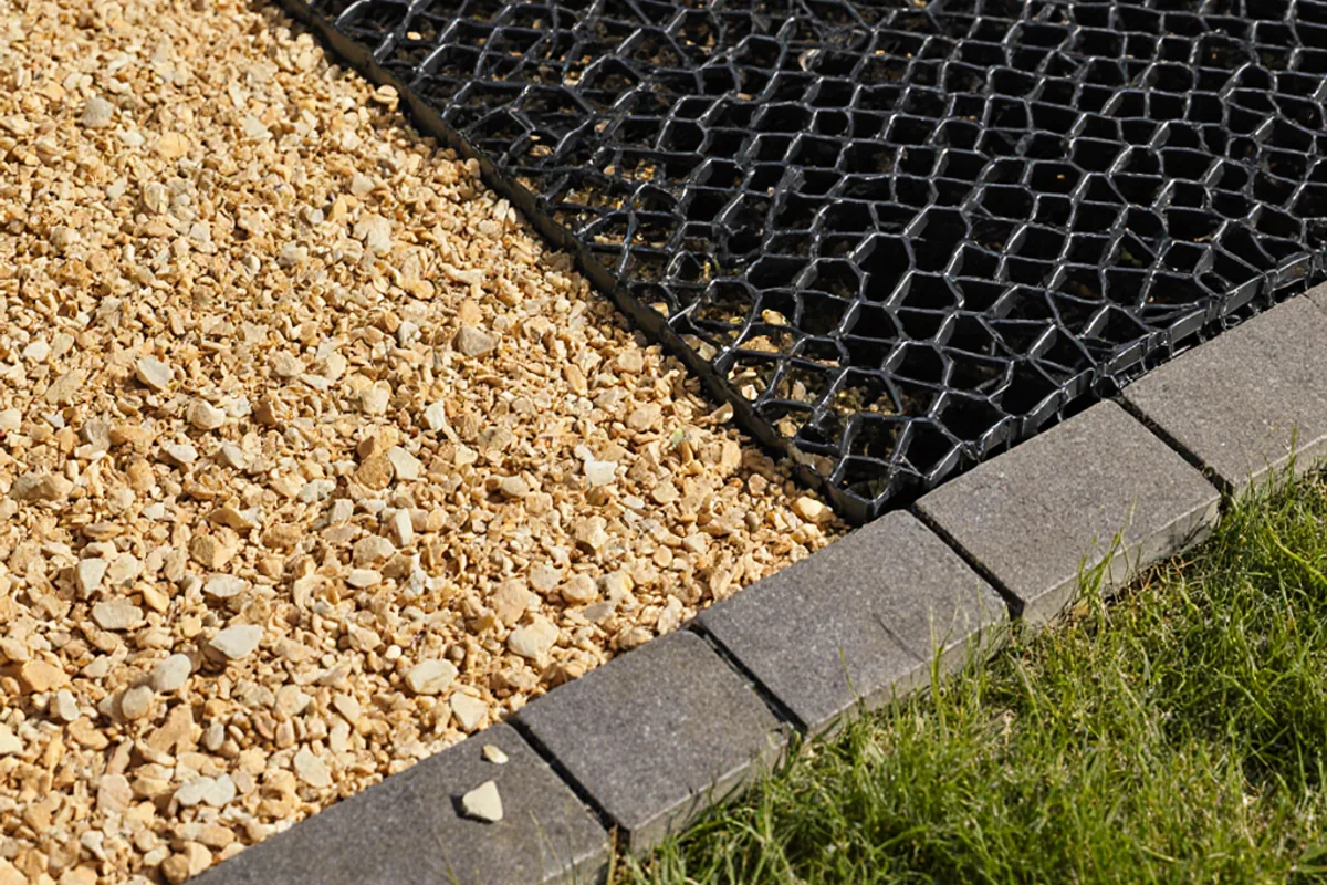 Golden driveway gravel meeting a charcoal edge with stabilising grid visible during installation